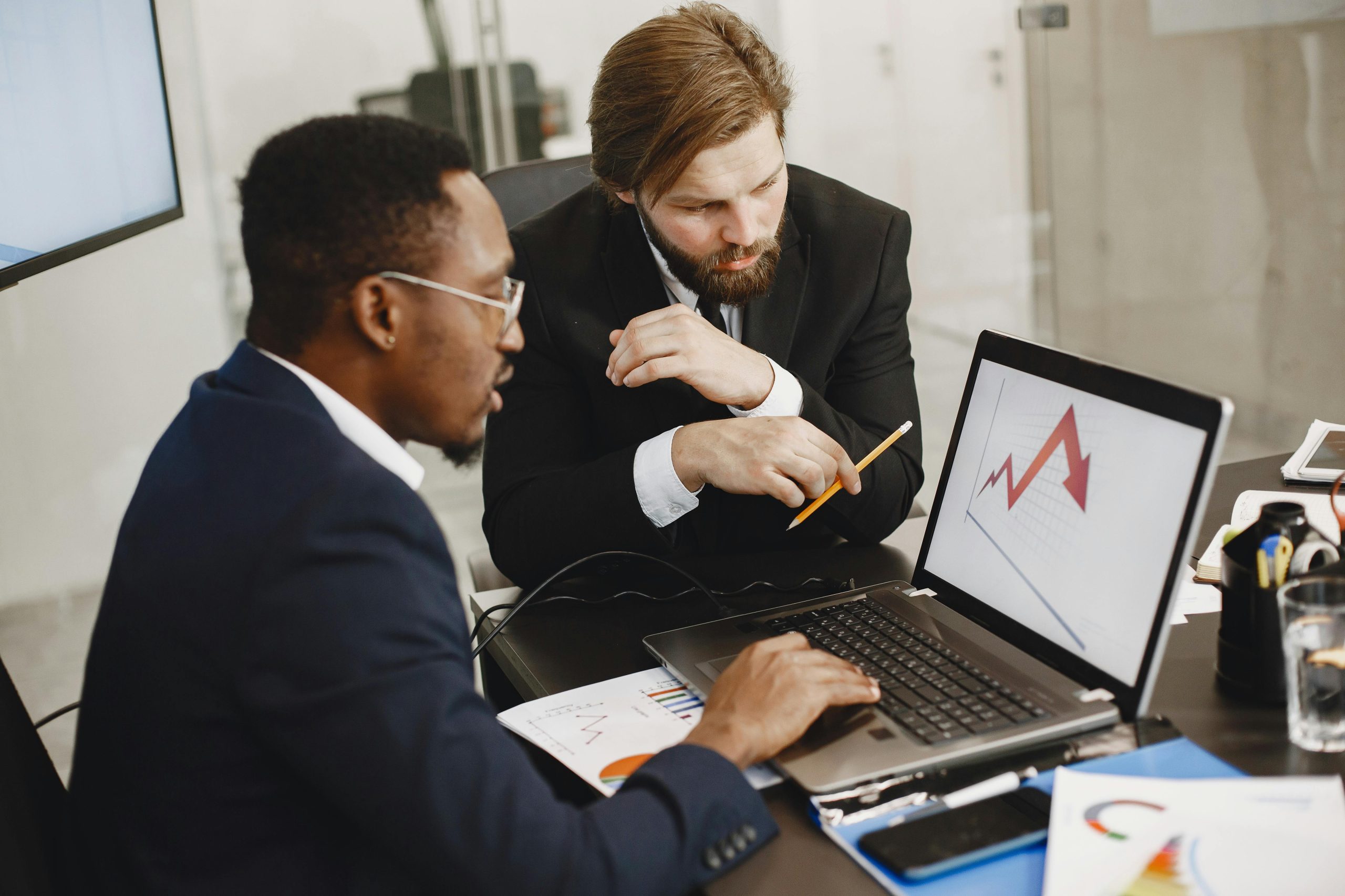 Two business professionals discuss marketing data on a laptop in a modern office.